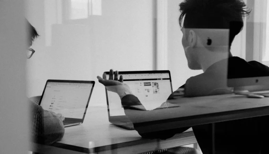 Two people discussing work on laptops, symbolizing overconfidence and misjudgment—key traits of the Dunning-Kruger effect.