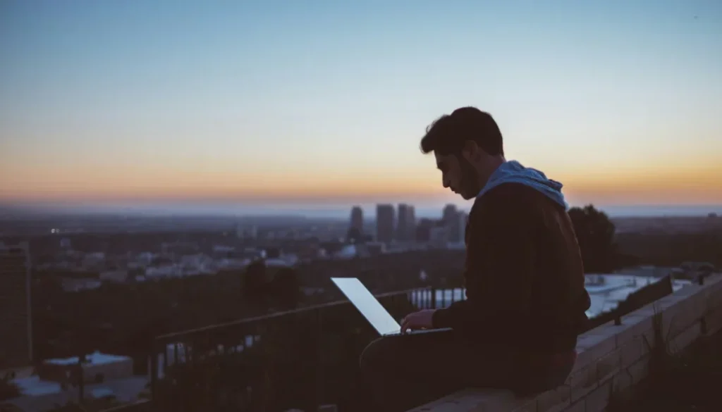 Man working on a laptop alone at sunset overlooking a city, representing focus and distraction-free deep work.