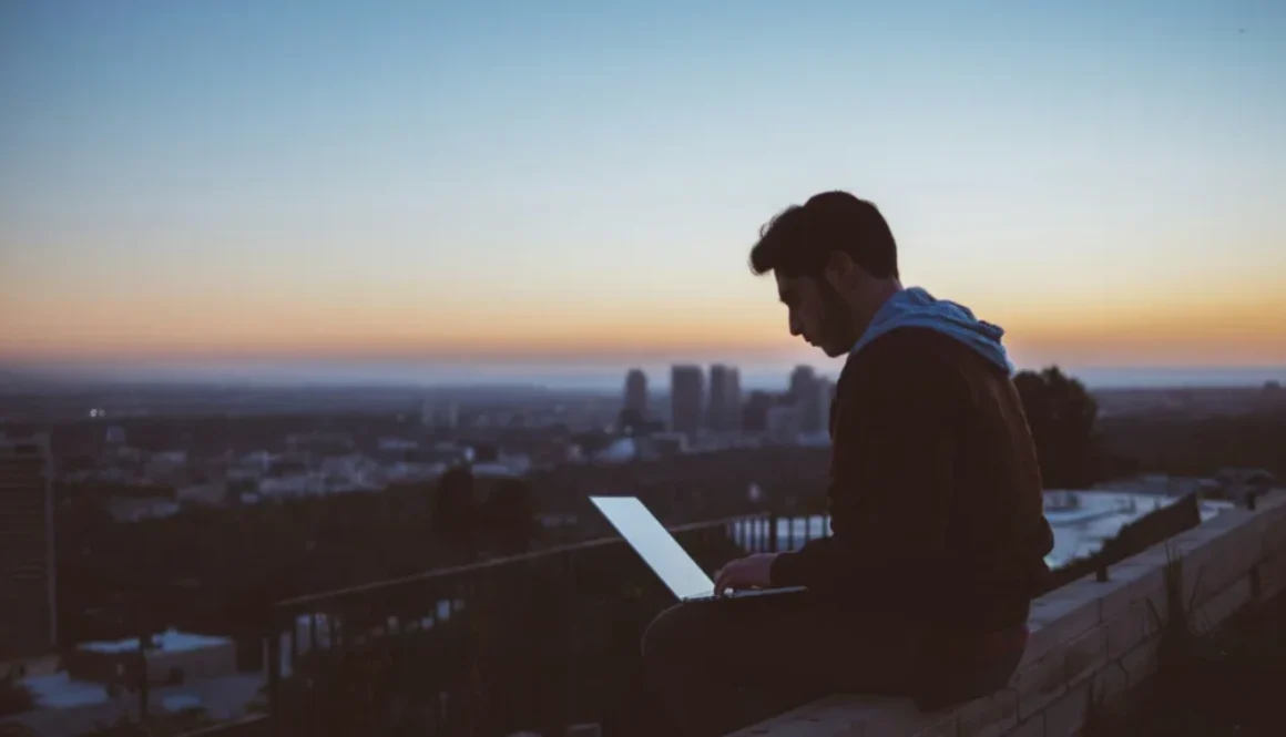Man working on a laptop alone at sunset overlooking a city, representing focus and distraction-free deep work.