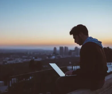 Man working on a laptop alone at sunset overlooking a city, representing focus and distraction-free deep work.
