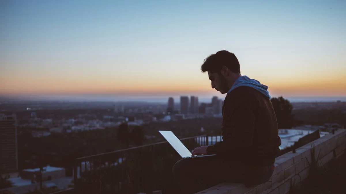 Man working on a laptop alone at sunset overlooking a city, representing focus and distraction-free deep work.