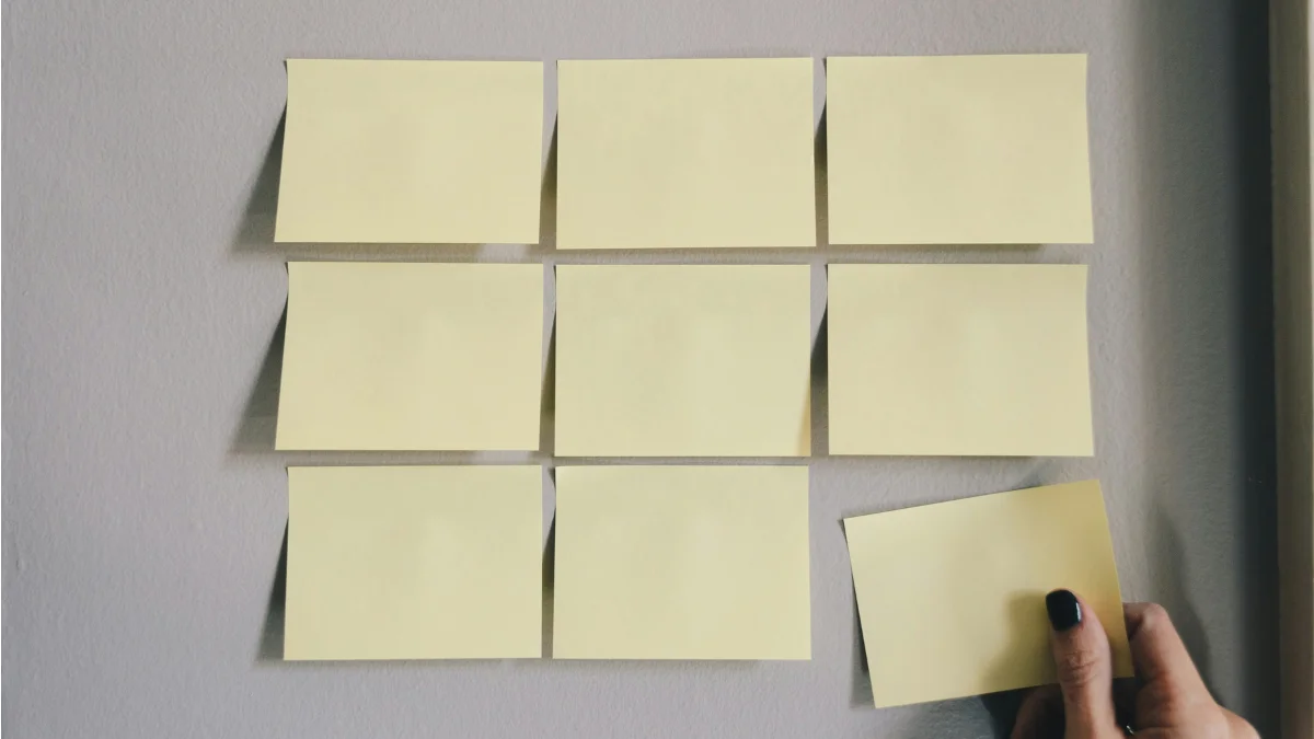 A hand placing the last sticky note on a grid of blank notes, symbolizing the Zeigarnik Effect—our tendency to remember unfinished tasks better than completed ones.