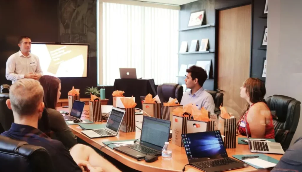 Team meeting with a presenter and laptops on the table, promoting open communication and feedback.