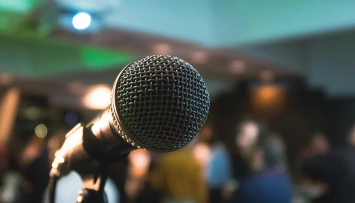 Close-up of a microphone with a blurred audience in the background, symbolizing public speaking and engaging with listeners.