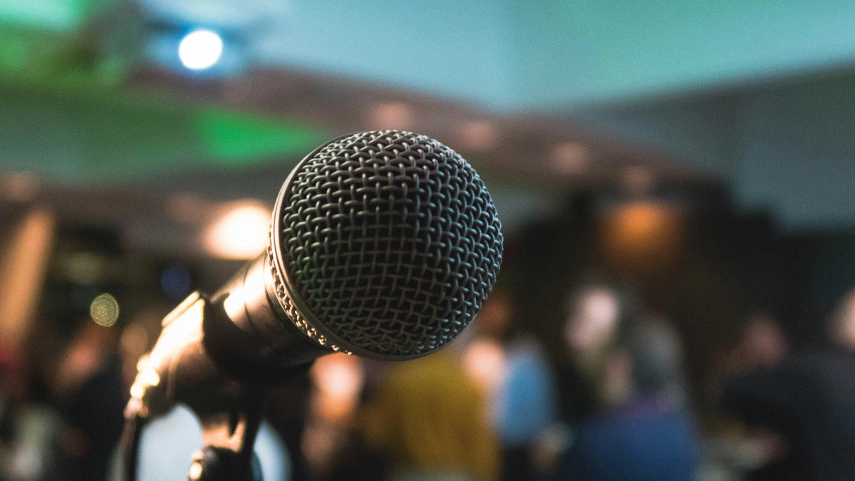 Close-up of a microphone with a blurred audience in the background, symbolizing public speaking and engaging with listeners.